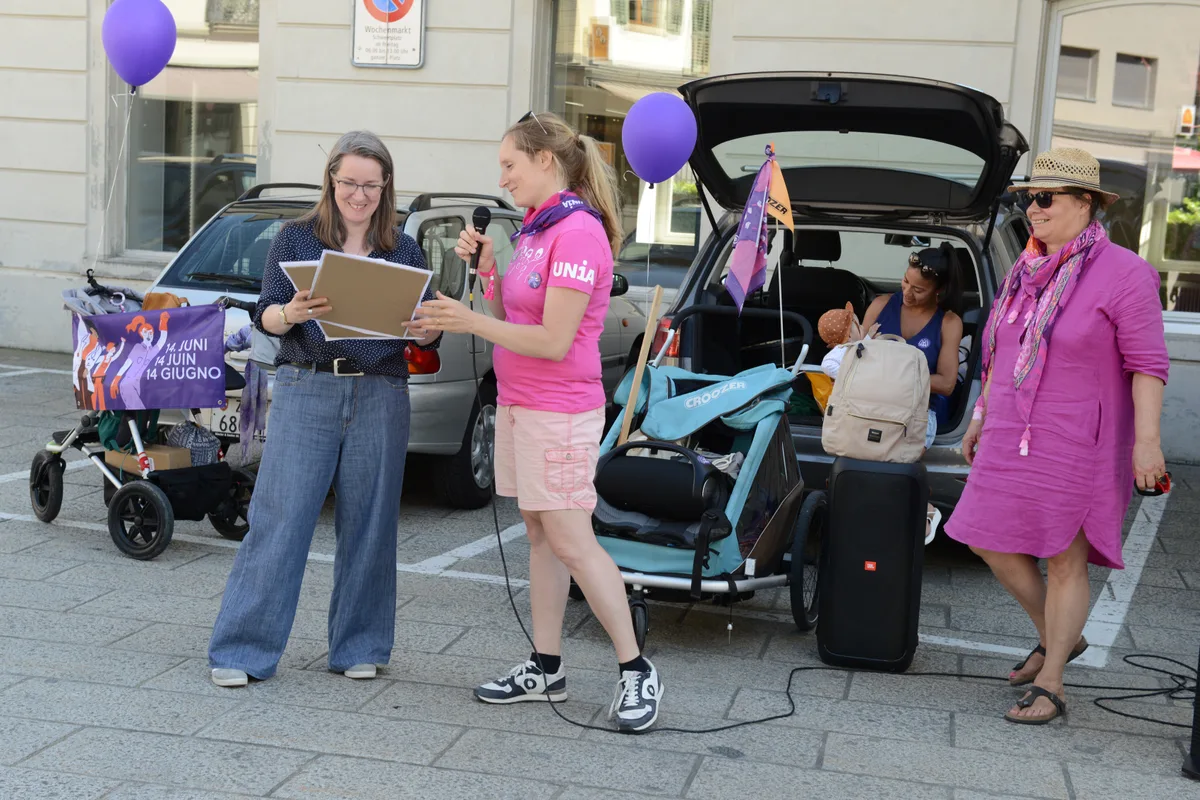 Laura Kieser (Mitte) überreicht die Forderungen des Streikkollektivs an Gemeinderätin Karin Eggenberger (links). Drei Frauen vor einem parkierten Auto. Eine Frau überreicht zwei Kartons mit Forderungen.